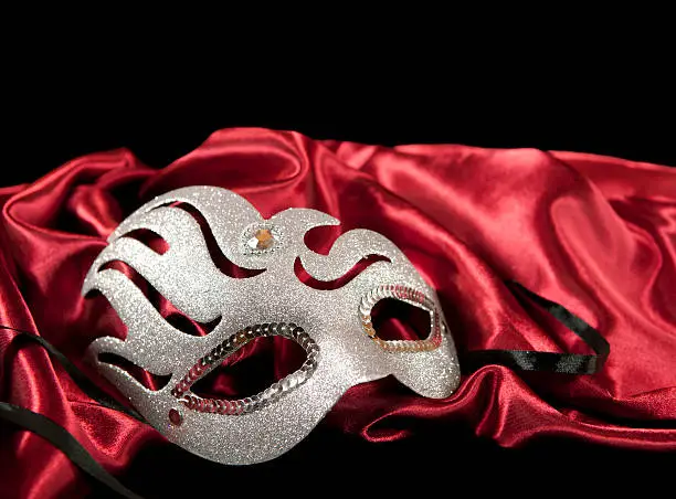 Melancholic venetian carnival mask with a red silk jacket against a black background.