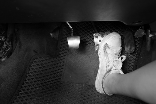 Teeanage girl foot in white canva shoe pushing the brake pedal of a manual car. There are cltuch, accelerator and brake pedals  on the automobile, inside a vehicle.