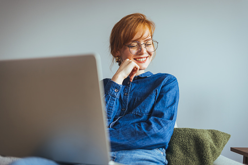 Smiling girl, student, professional employee, typing on laptop, sitting at home on comfortable sofa, happy woman learning e-learning software online using technology app for work education concept