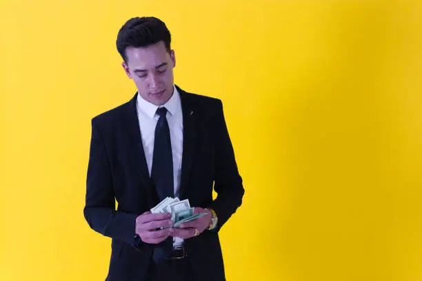 Photo of A dapper man dressed in suit looking at a wad of bills that holds with his hands