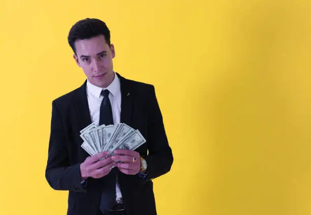 Photo of shaven-face handsome man dressed in suit looking at camera with a wad of bills in his hands