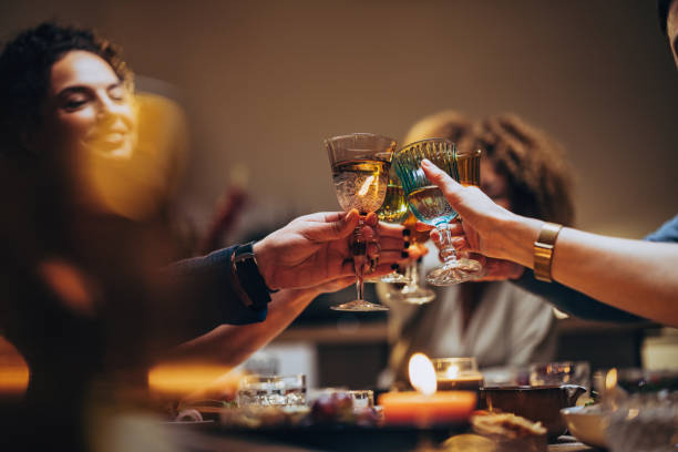 Friends Toasting With A Glass Of Wine During A Dinner Celebration Unrecognizable group of multi-ethnic people having fun at dinner party and toasting with alcohol. evening meal stock pictures, royalty-free photos & images
