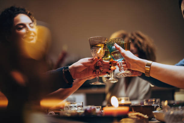 Friends Toasting With A Glass Of Wine During A Dinner Celebration Unrecognizable group of multi-ethnic people having fun at dinner party and toasting with alcohol. toasting stock pictures, royalty-free photos & images
