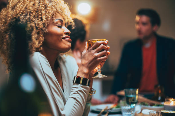 une femme heureuse déguste un verre de vin lors d’un dîner entre amis - champagne flute champagne black wineglass photos et images de collection