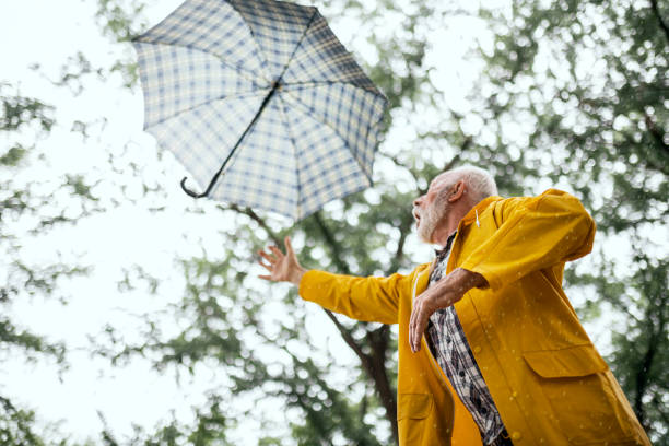 istock Senior man on a windy rainy day losing his umbrella 1400586782