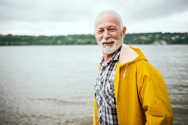 istock Senior man walking on a raining day along river wearing yellow raincoat looking at camera 1400586940