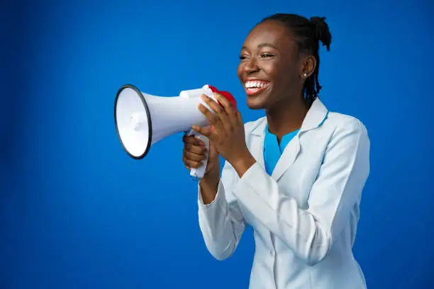 Photo of Afro american female doctor in white medical gown scream in megaphone in studio