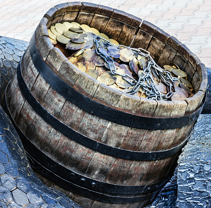 A lot of coins and chain in a wooden barrel