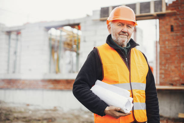 istock Senior man engineer or construction worker in hardhat standing with  blueprints at building new modern house. Male architect or contractor checking plans at construction site. Copy space 1400591119