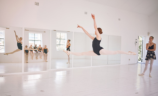 Young woman dance instructor teaching a ballet class to a group of a children in her studio. Ballerina teacher working with girl students, preparing for their recital, performance or upcoming show