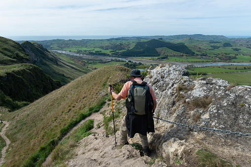 Man hiking Te Mata Peak track, holding chain to descent steep downhill, views of Hawke's Bay.