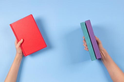 Hands holding books over light blue background. Education, self-learning, book swap, sharing, bookcrossing concept.