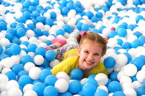 Little happy girl playing in dry pool with plastic balls. Close-up leisure activities indoors. Playground
