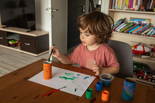 Little boy painting on toilet paper roll and paper at home