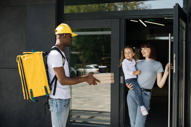 istock Smiling African American delivery man in yellow uniform cap delivering cardboard boxes with pizza 1400599653