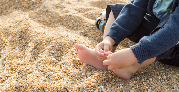 Child playing with the toes and feeling the texture of the beach sand, sensory experience.