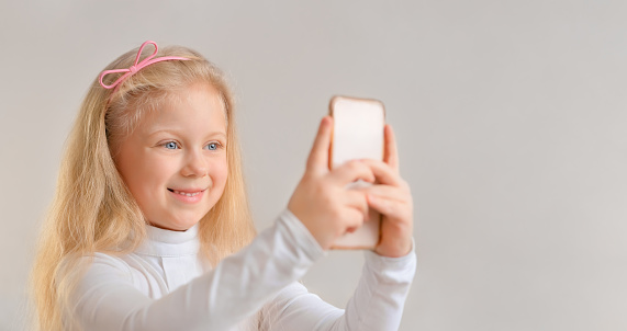 Beautiful smiling blonde little girl taking a selfie photo with smartphone