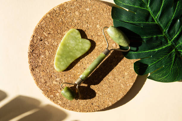 istock Jade Gua sha scraper and face roller massager on a cork round stand with a monstera leaf. 1400603610