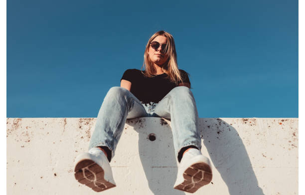 istock Young Woman Sitting on Concrete Wall With Sunglasses 1400603906