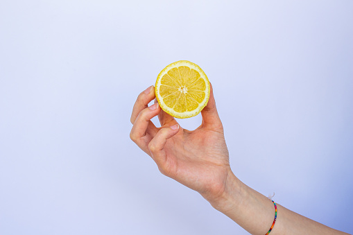 Closeup hand holding half lemon, isolated on white background.