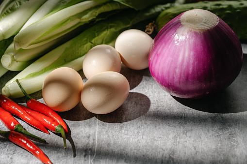 Various raw and fresh vegetable ingredients for cooking in front of a tiled kitchen wall.