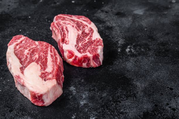Raw chuck eye roll steaks, premium beef meat on a butcher board. Black background. Top view. Copy space