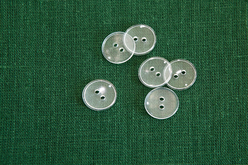 Natural green linen fabric on which are transparent, flat buttons.