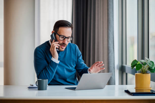 istock Worried businessman discussing on cellphone while working on laptop at desk 1400610585