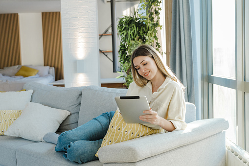 Young woman relaxing on the couch and consuming internet content on digital tablet