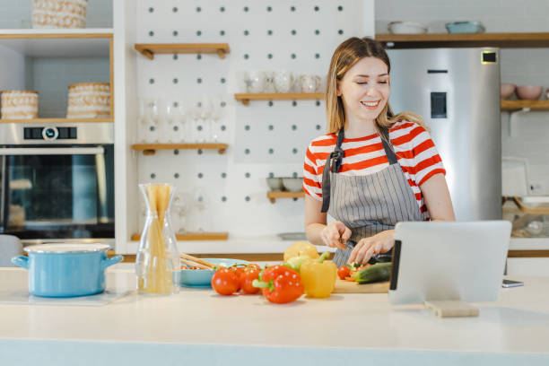 istock Beautiful woman cutting ingredients for a meal in the kitchen while looking at digital tablet 1400612074