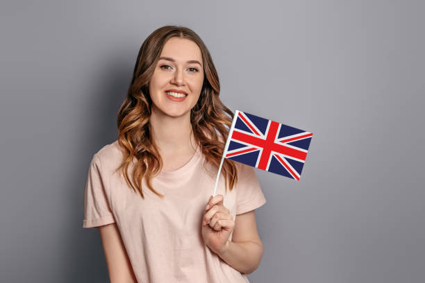 istock Education abroad. Female student holds a small British flag isolated over grey background. student exchange 1400612093