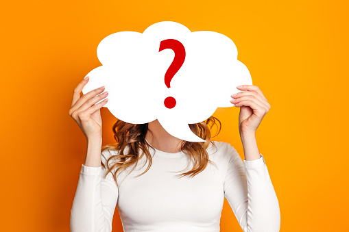 girl wearing white t-shirt holding paper card bubble with question mark isolated over orange background