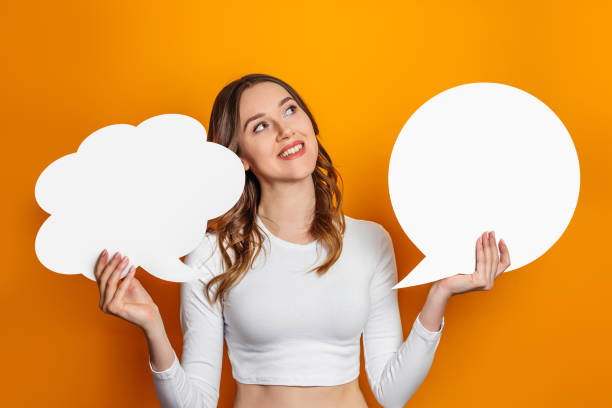 istock young woman holds two blank speech bubble isolated on an orange background. Student holding a paper cloud. Copy space 1400612115