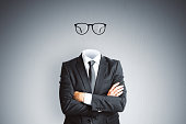 Headless invisible businessman in suit with folded arms and abstract glasses standing on gray wall background. Business and secret concept.
