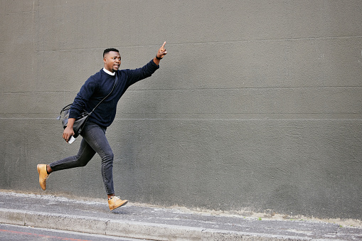 African american businessman travelling alone and rushing for a taxi  in the city. Black male running and waving for a taxi while on his way to work in the morning
