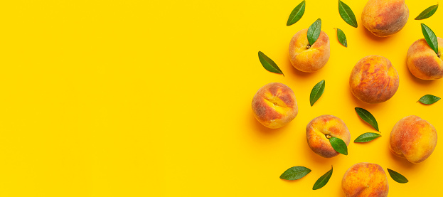 Summer fruit background. Flat lay composition with peaches. Ripe juicy peaches with green leaves on yellow background. Flat lay top view copy space. Fresh organic fruit, vegan food. Harvest concept.