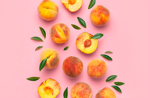 Summer fruit background. Flat lay composition with peaches. Ripe juicy peaches with green leaves on pink background. Flat lay top view copy space. Fresh organic fruit vegan food. Harvest concept.