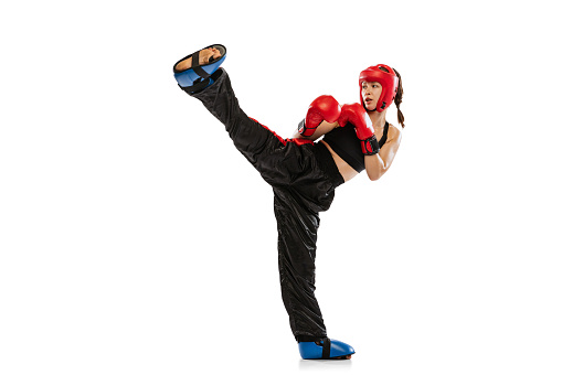 High kick. One female boxer in boxing gloves and helmet training isolated on white studio background. Sport, competition, hobby, results, success concept. Sportive woman practicing in boxing.