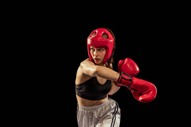 istock Professional female boxer in boxing gloves and helmet training isolated on dark studio background. Sport, competition, hobby, results, success concept 1400615736