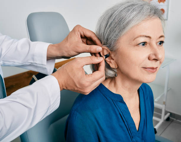 Senior woman during installation hearing aid into her ear by her audiologist, close-up. Hearing treatment for hearing impaired people stock photo
