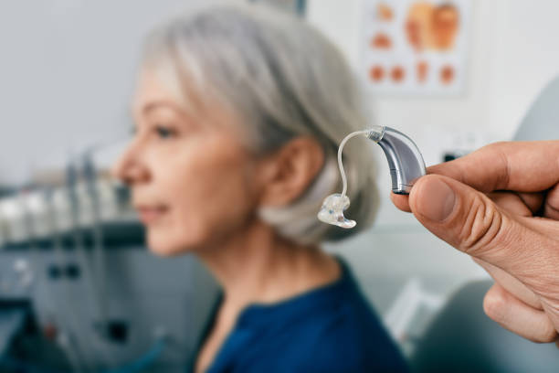 Close-up of hearing aid near senior patient's ear at audiology clinic. Hearing solutions, hearing BTE aids stock photo