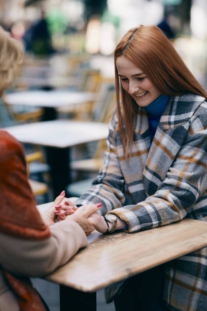 une grand-mère qui tisse des liens avec sa petite-fille tout en étant assise dans un café et en se tenant la main. - generation gap multi generation family vertical holding hands photos et images de collection