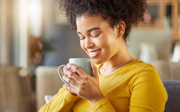 joven y feliz mujer de raza mixta sosteniendo y bebiendo una taza de café en casa. una acogedora mujer hispana sonriendo y disfrutando de una taza de té mientras se relaja en casa - women solitude enjoyment 20s fotografías e imágenes de stock