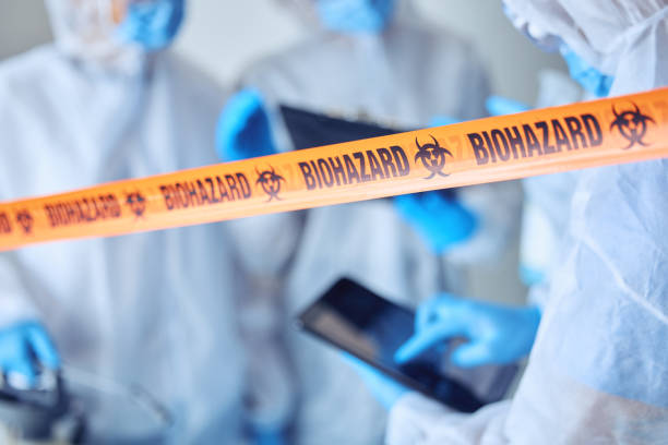 istock Closeup on biohazard quarantine tape. Hands of scientist using a digital tablet behind covid barrier. Medical professional working in a biohazard crime scene. Doctors working behind caution tape 1400620483