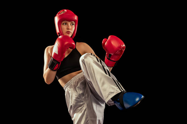 Knee kick. Female boxer in boxing gloves and helmet training isolated on dark background. Sport, competition, hobby, results, success concept. Sportive girl practicing in boxing. Copy space for ad