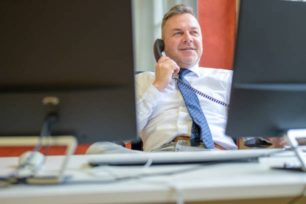 Confident businessman talking on a telephone in an office as he relaxes sitting slumped back in his chair