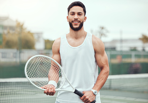 Portrait of smiling mixed race tennis player holding racket on court. Happy fit hispanic professional standing alone and feeling confident in sports club. Ready for an athletic match and healthy game