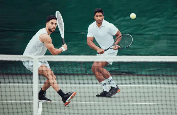 Two ethnic tennis players holding rackets and playing game on a court. Serious, focused team of athletes together during match. Playing competitive doubles match for fitness and health in sports club