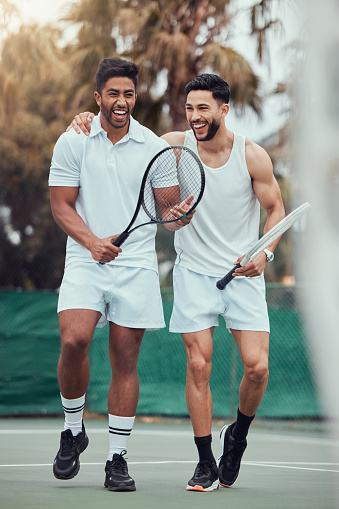 Full length two ethnic tennis players holding rackets and bonding playing court game. Smiling athletes team together after match. Play competitive doubles match for fitness and health in sports club