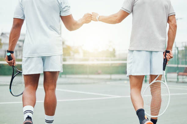 deux joueurs de tennis ethniques inconnus donnant un coup de poing avec le poing avant de jouer au jeu sur le court. faites correspondre l’équipe d’athlètes debout et en utilisant le geste de la main pour avoir de la chance. jouez à un match de spor - two pairs photos et images de collection